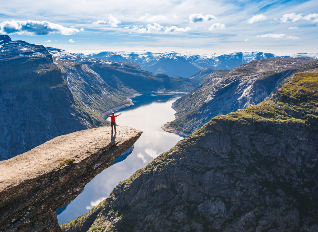 Young woman relaxon Trolltunga. Happy girl enjoy beautiful lake and